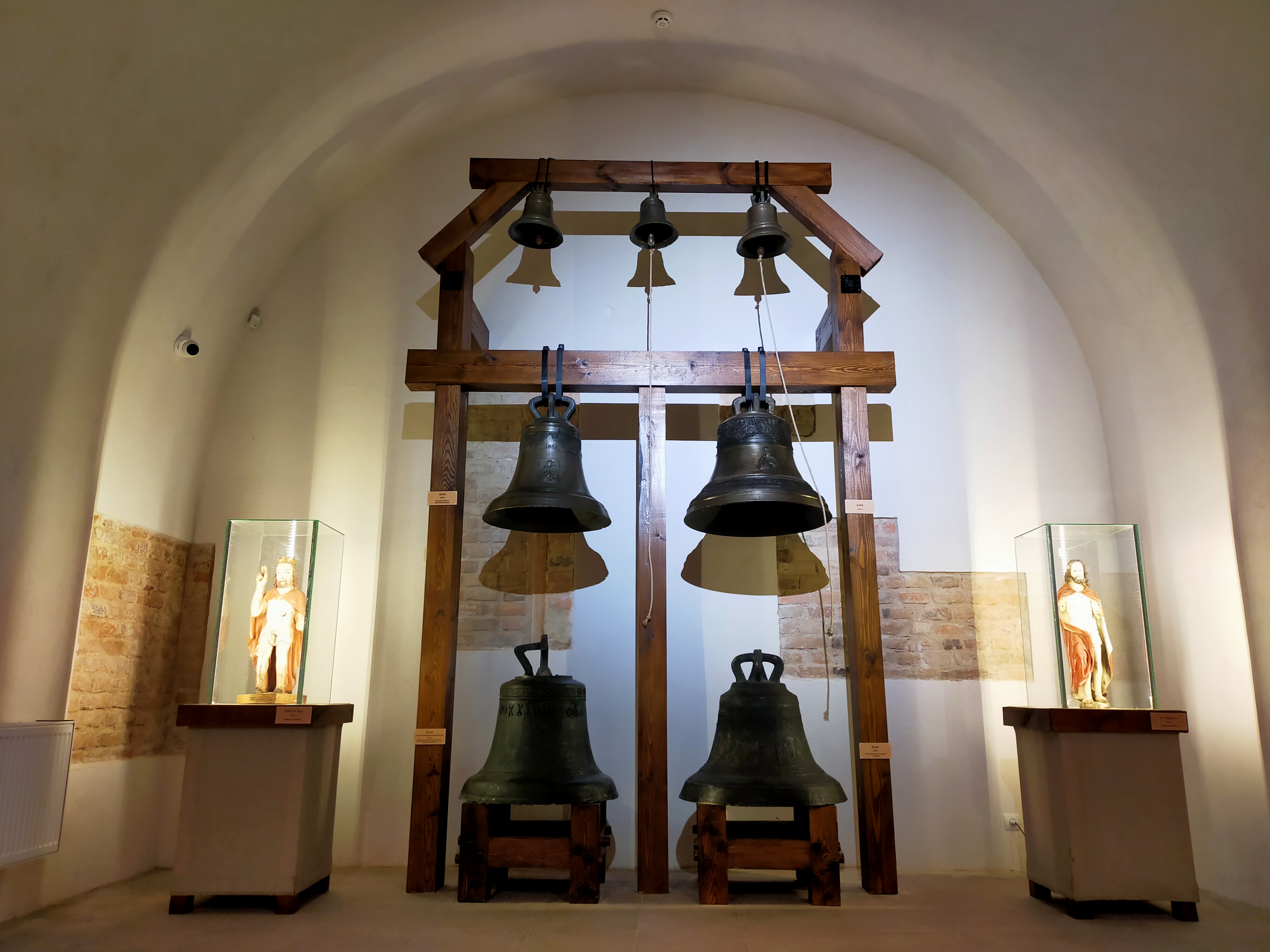The picture shows 3 small bells in the mountain, 4 large ones raised, wooden sculptures placed on both sides of the bells. xhibition - Our spiritual treasures
